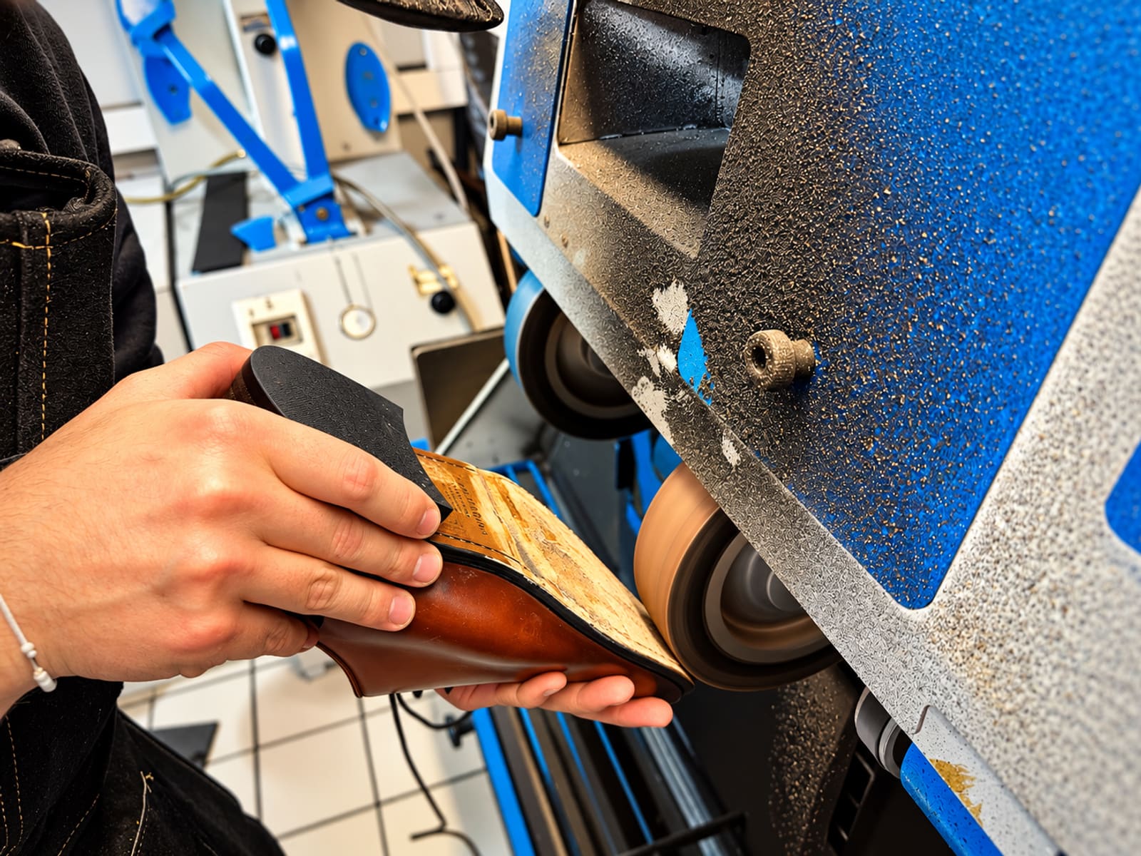 Artisan ponçant la semelle d'une chaussure sur une bande abrasive, atelier JT2A